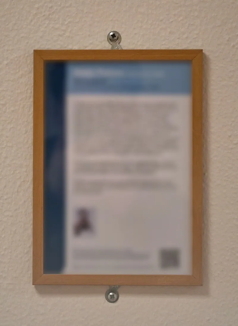 Een ingelijst infobordje met een lange tekst, naast een kunstwerk aan de muur; de tekst is onscherp gemaakt